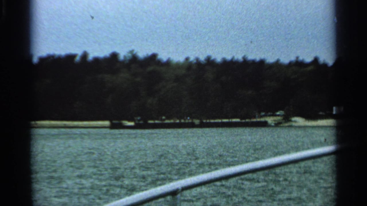 1964 Washington Island lakeside view from a boat, with white railing, rippled water, wooded shore, and pale sky.