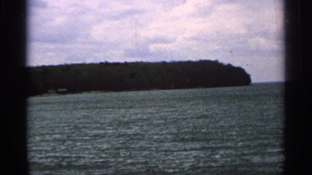 1964 Washington Island home-movie view of a wooded shoreline seen across rippling water from a moving boat.