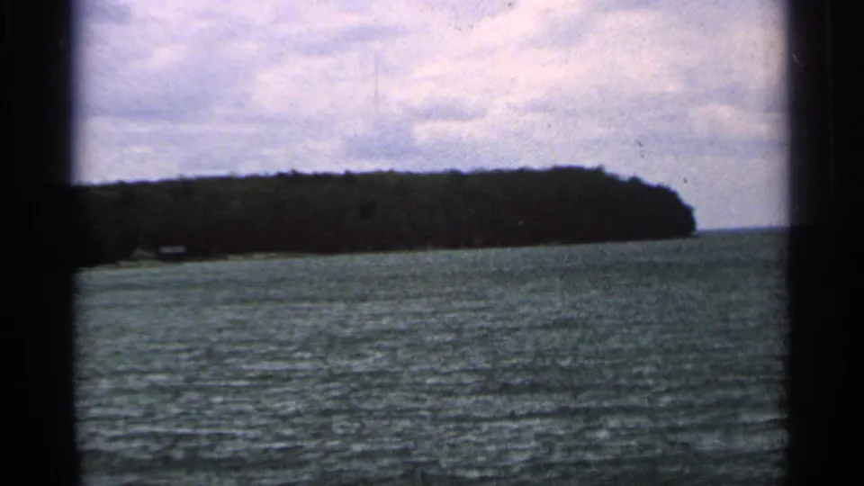 1964 Washington Island home-movie view of a wooded shoreline seen across rippling water from a moving boat.