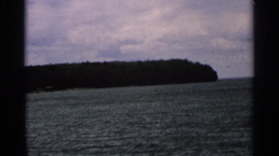Washington Island shoreline appears beyond open lake water, framed by dark boat or film edges in 1964 8mm footage.