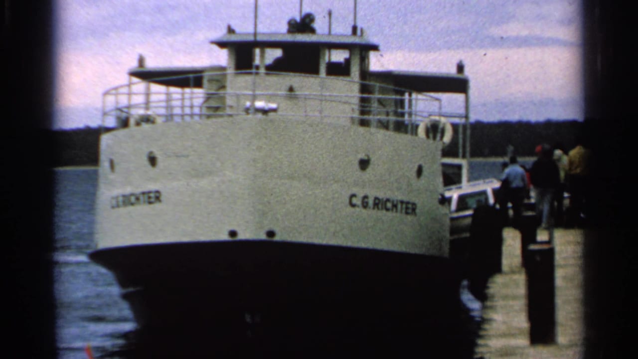 1964 8mm view of the C.G. Richter ferry at a Washington Island dock with people standing near the boarding area.