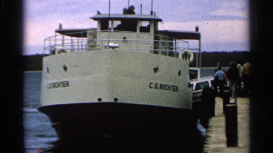 1964 8mm view of the C.G. Richter ferry at a Washington Island dock with people standing near the boarding area.