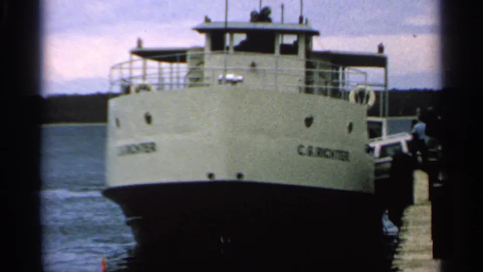 Front view of the white C.G. Richter ferry beside a dock, with water and shoreline behind it in 1964 Wisconsin footage.