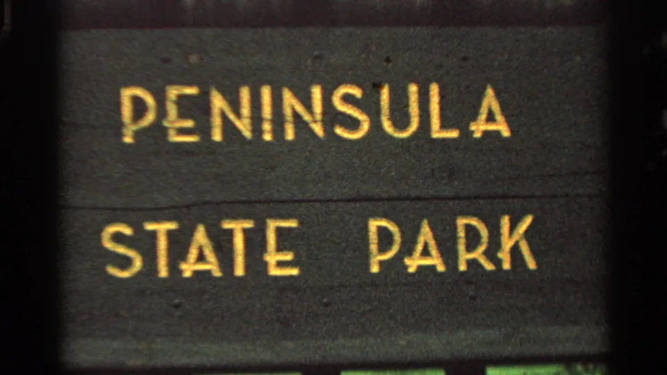Close 8mm frame of a dark sign with yellow letters reading PENINSULA STATE PARK, supporting the Wisconsin travel context.