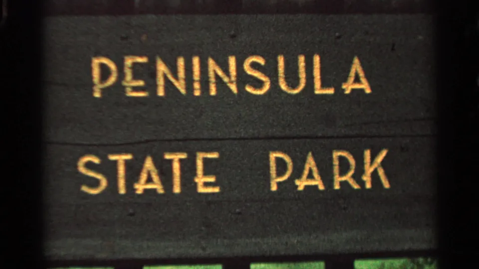 1964 Wisconsin 8mm frame showing a close-up of a dark Peninsula State Park sign with gold lettering and film edges.