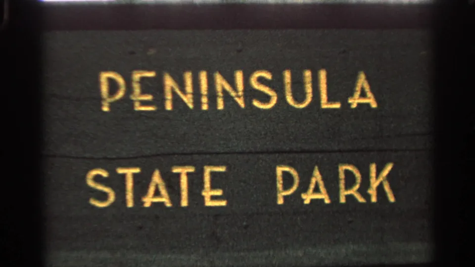 1964 Wisconsin home-movie frame with the Peninsula State Park sign centered in soft 8mm focus.