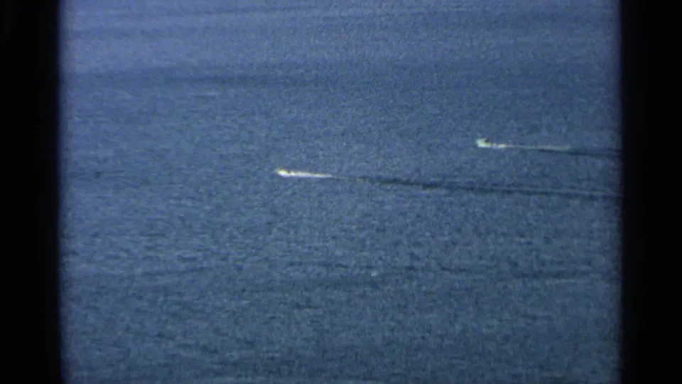 Aerial 8mm frame showing two small white boats crossing the water near Washington Island, Wisconsin, with dark wakes trailing behind them.