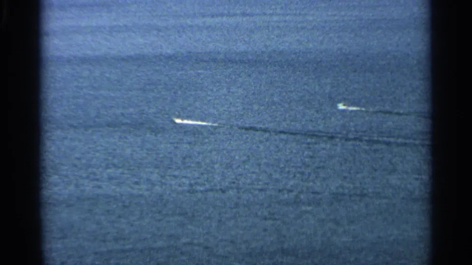 Final aerial frame of two small boats on the water near Washington Island, Wisconsin, with long wake trails and visible 8mm film texture.