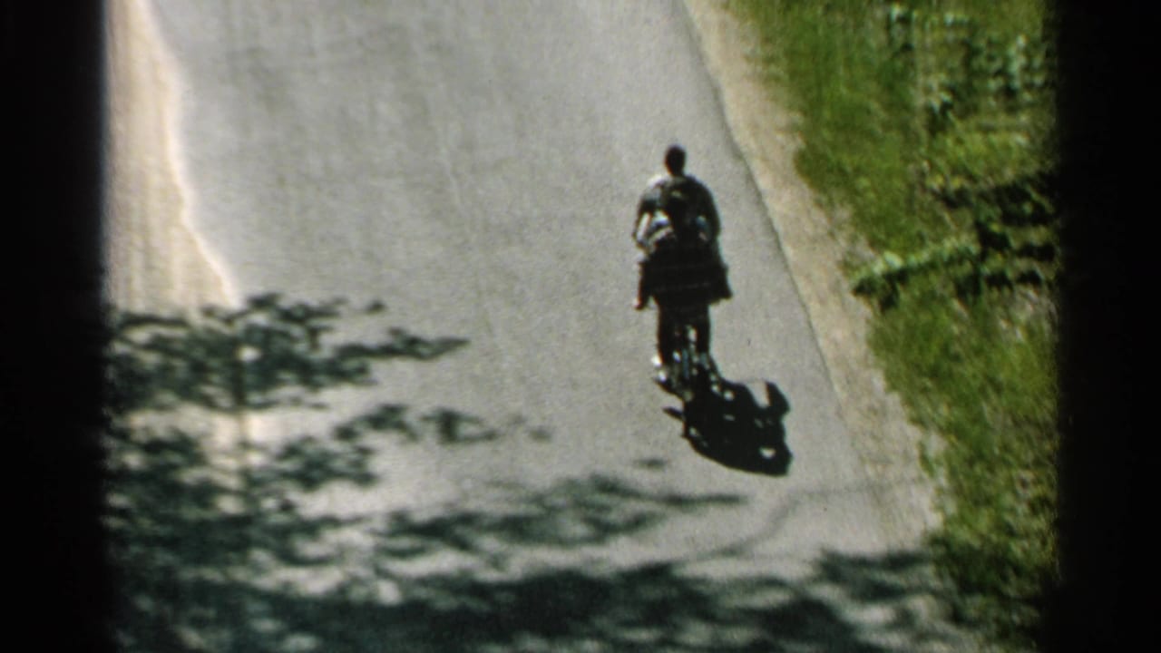 Two people ride one bicycle down a quiet paved road with long shadows.