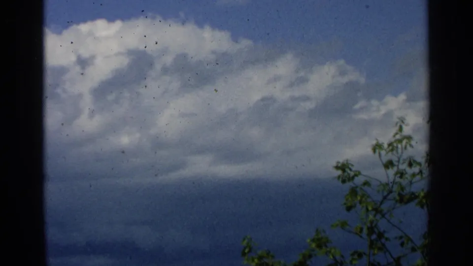 Washington Island home-movie frame of cloud cover over blue lake water, with leaves and film specks visible.