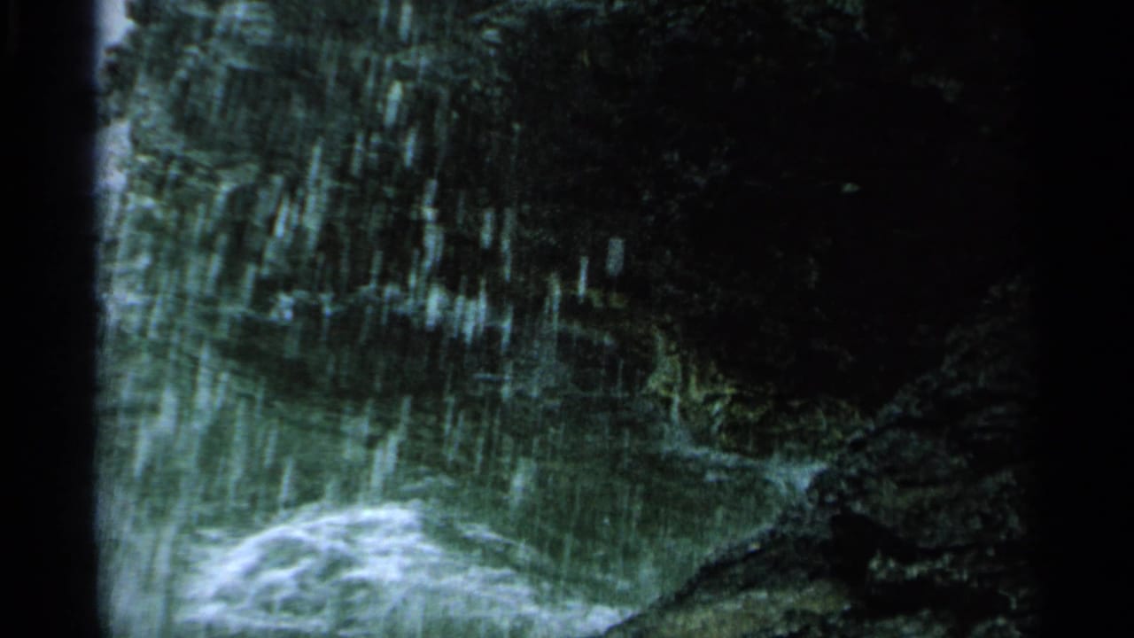 1964 Washington Island 8mm frame of greenish water and white foam moving through dark shoreline rocks.