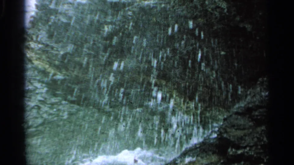 1964 Washington Island 8mm frame with water spray falling across dark rocks as waves break below.