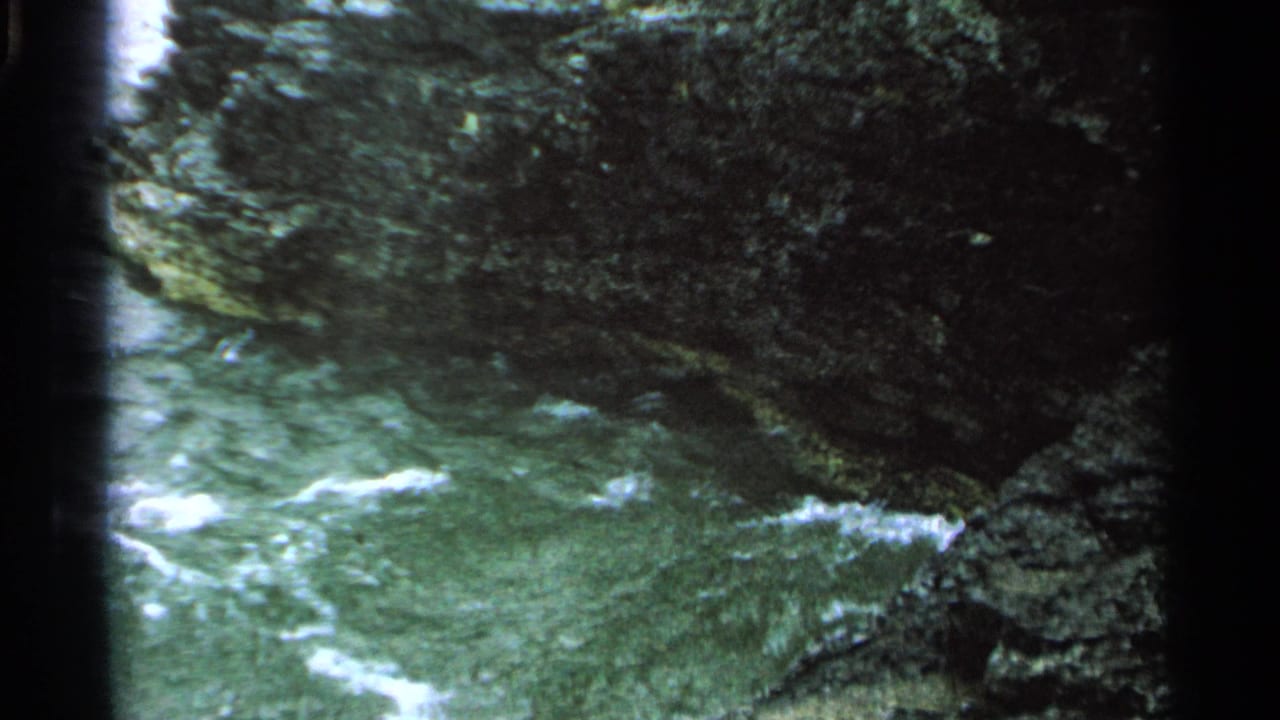 Water swirls below dark rocky shoreline with white foam near the edge.