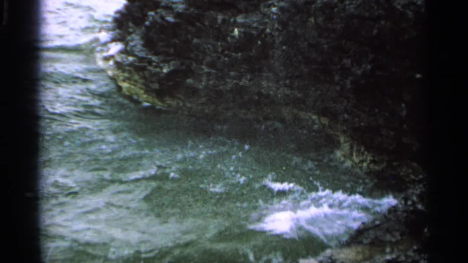 Green-tinted 8mm view of water surging between dark Washington Island rocks, with small whitecaps and foam near shore.