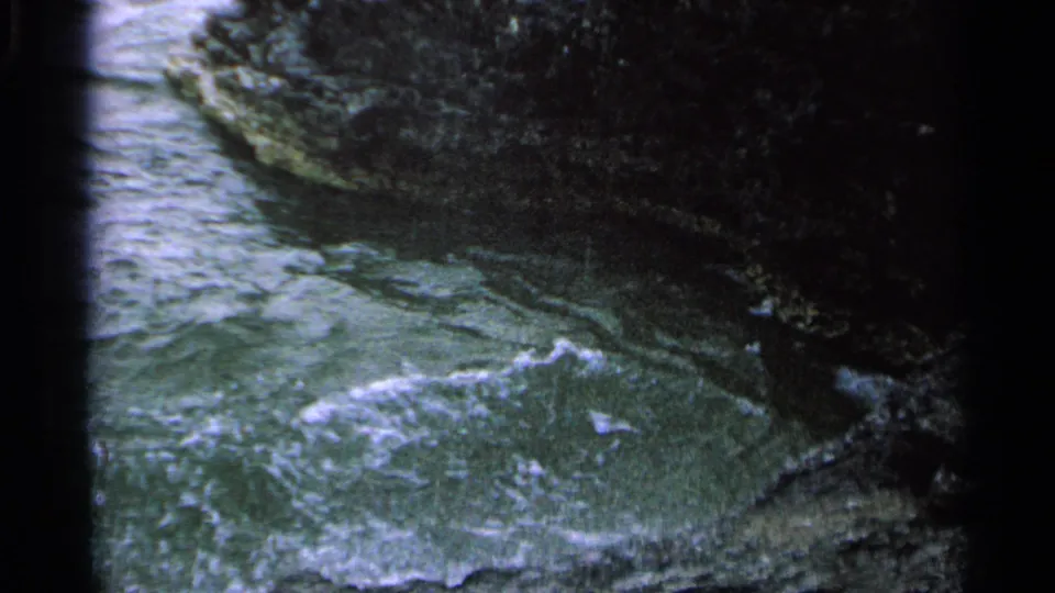 Handheld 8mm frame of foamy water moving around dark, mossy rocks on the Washington Island shoreline.