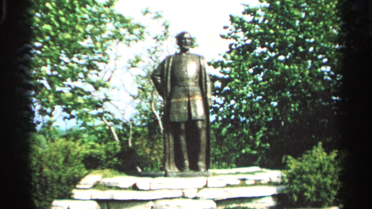 Jean Nicolet statue on a stone base at Washington Island, Wisconsin, framed by trees in 1964 8mm footage.