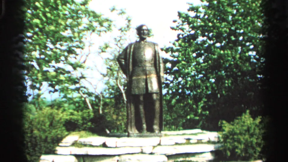 Jean Nicolet statue on a stone base at Washington Island, Wisconsin, framed by trees in 1964 8mm footage.