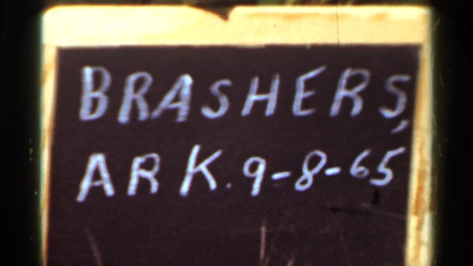 1965 Arkansas 8mm frame of a handwritten chalkboard sign reading BRASHERS, ARK. 9-8-65 within a yellow border.