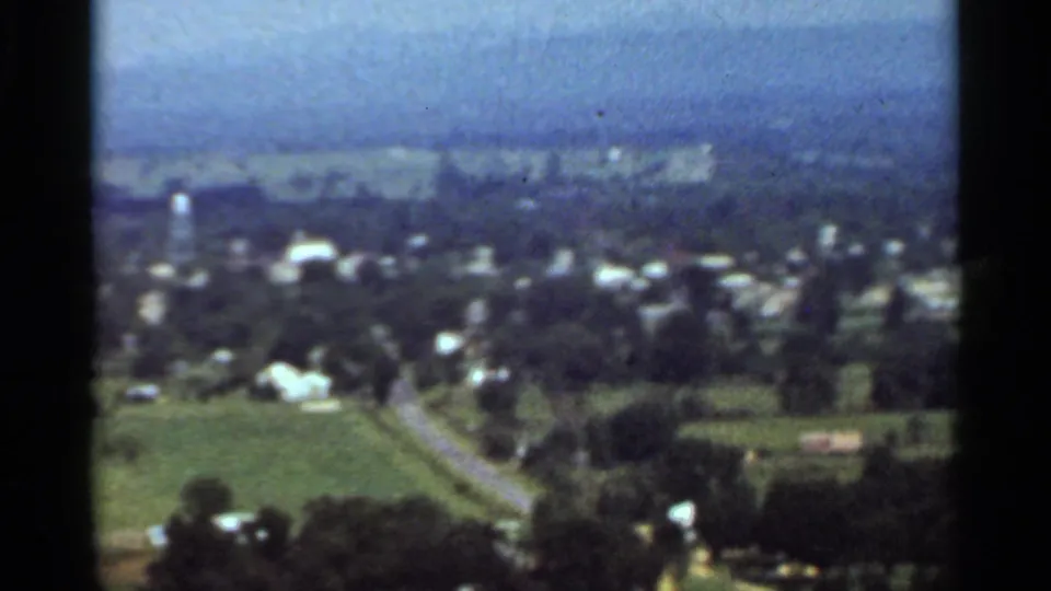 1965 Arkansas home-movie view looking over Danville, with houses, green fields, roads, trees, and a hazy blue sky.