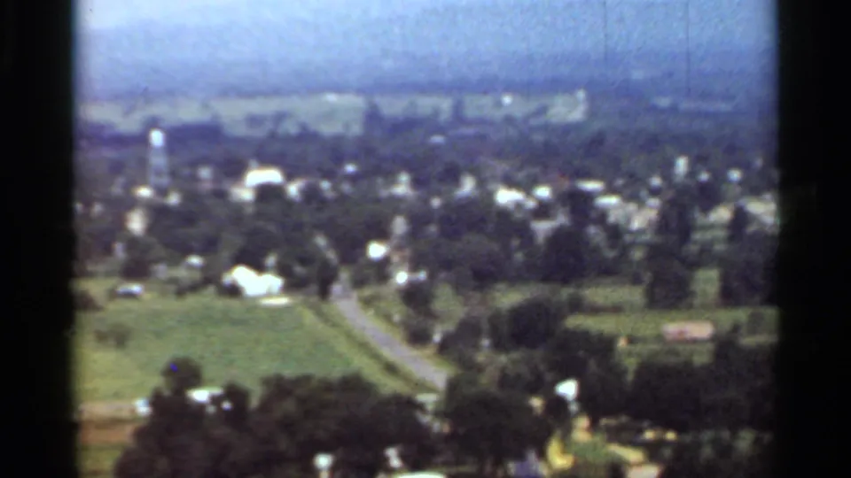 1965 Arkansas wide view of Danville from above, showing homes, fields, roads, a water tower, and scattered white buildings.