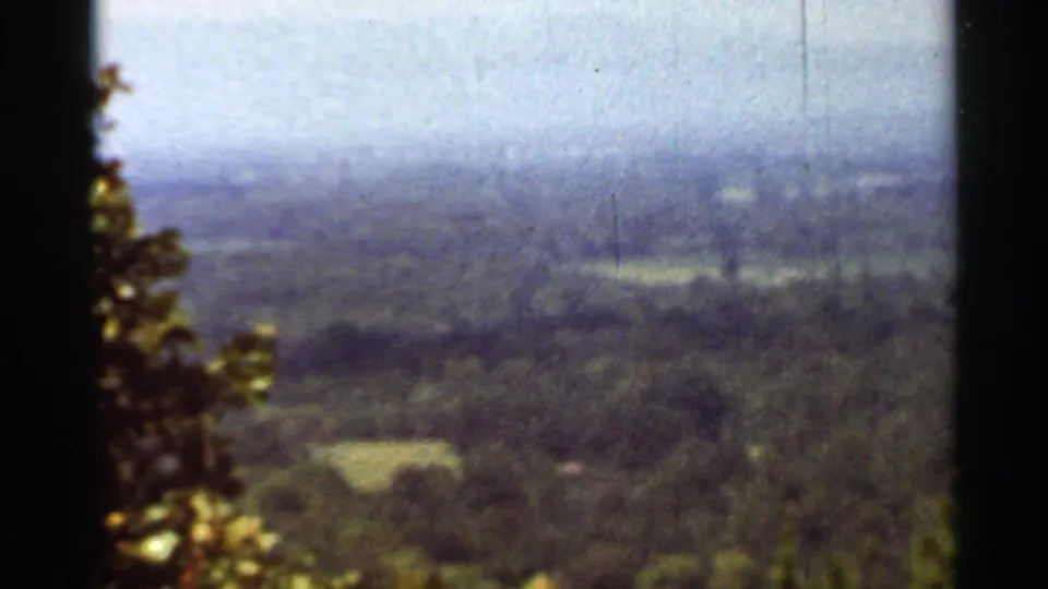1965 Arkansas 8mm frame showing a hazy mountain overlook with wooded hills, distant valley, and dark film edges.