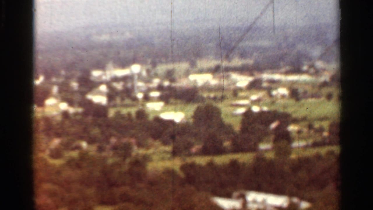 Distant small town, fields, and wooded slopes seen from above.