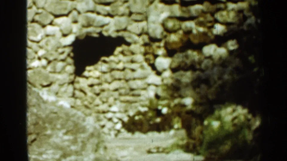 Handheld 8mm view of the Arkansas stone ruin, with the black arched opening centered amid rough rocks and brush.