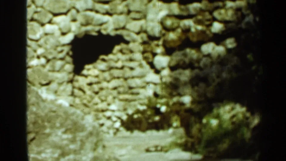 Final 1965 Arkansas frame of the stone cave-like opening, with shrubs and dark film border visible along the side.