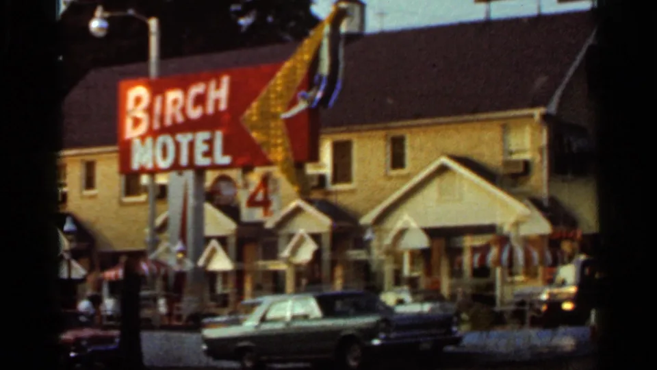 Wider 1965 Arkansas roadside view of the Birch Motel sign, motel frontage, parked cars, and porch details.