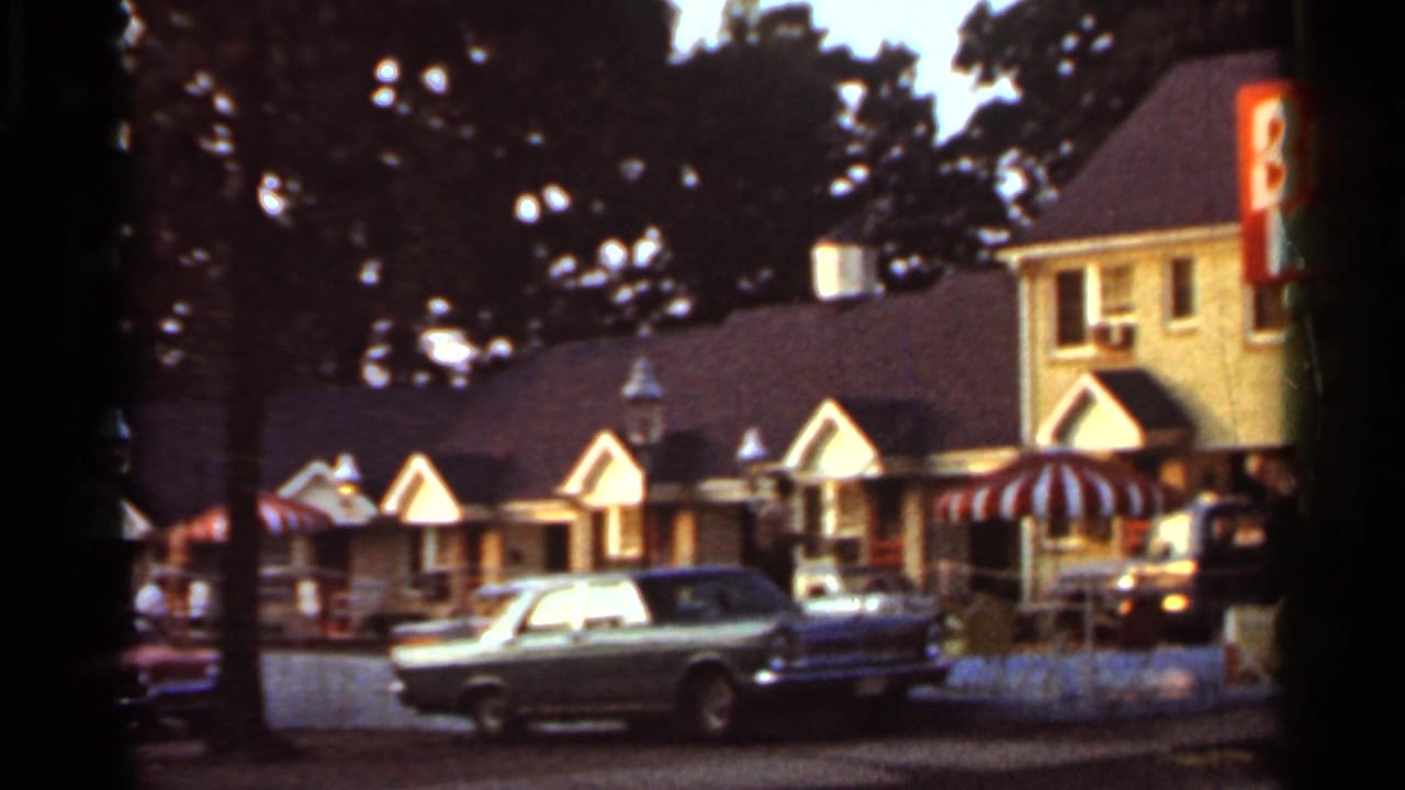 1965 Arkansas roadside amusement area with A-frame shop fronts, striped awnings, a parked classic car, and partial vertical signage.