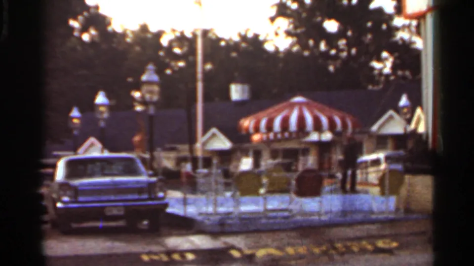1965 Arkansas 8mm frame showing a roadside motel exterior with striped awning, vintage car, lamps, and dusk sky.