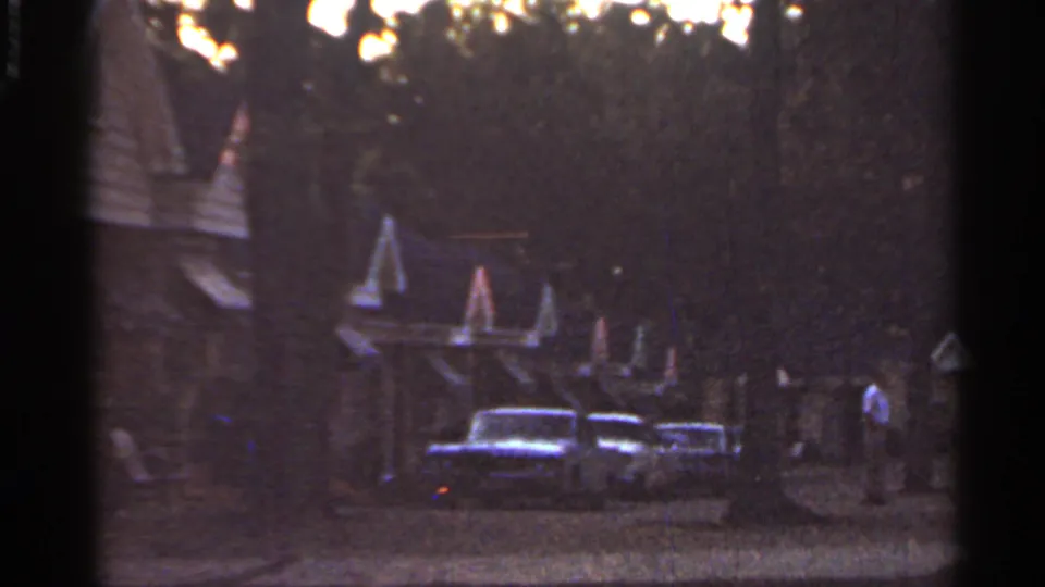1965 Arkansas roadside motel at dusk, with parked cars, peaked architectural details, trees, and a person near the walkway.