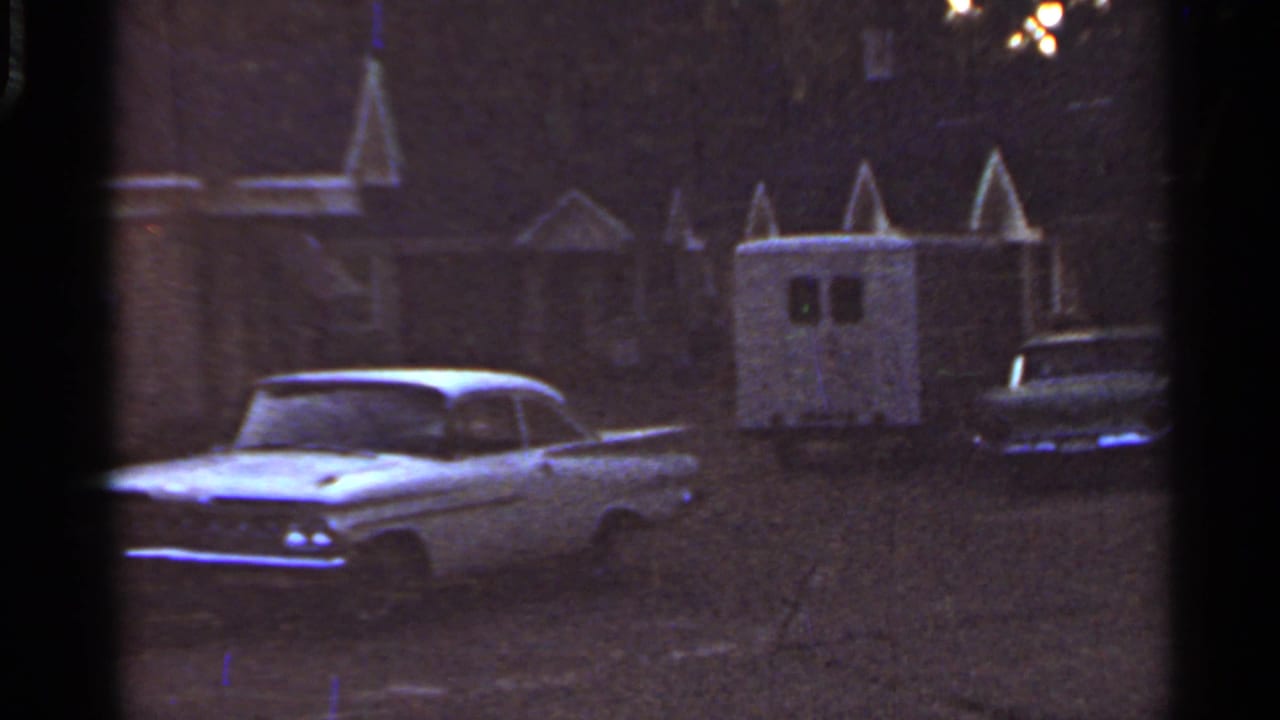1965 Arkansas 8mm frame showing a white parked car, small trailer, and dim suburban house exteriors.