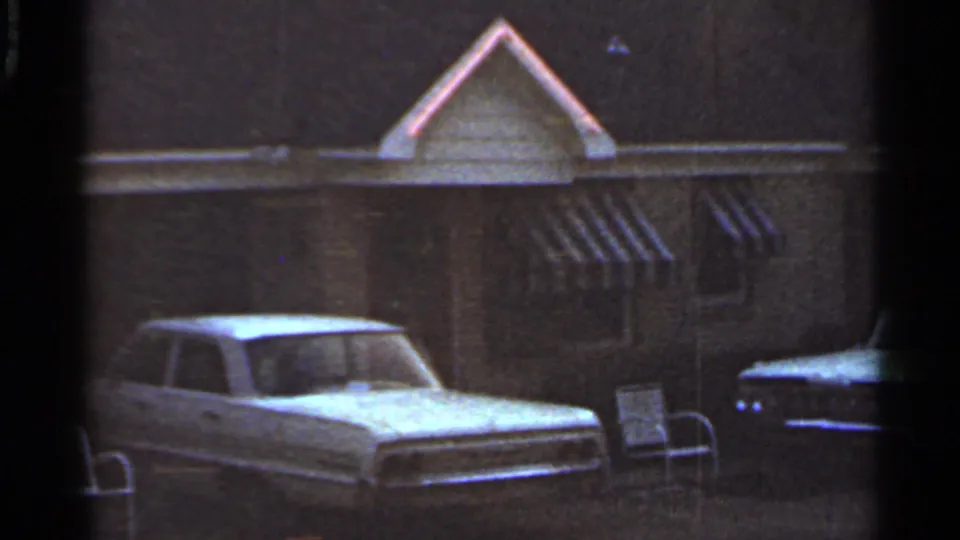 1965 Arkansas 8mm frame showing a white car near a modest house facade with striped awnings.