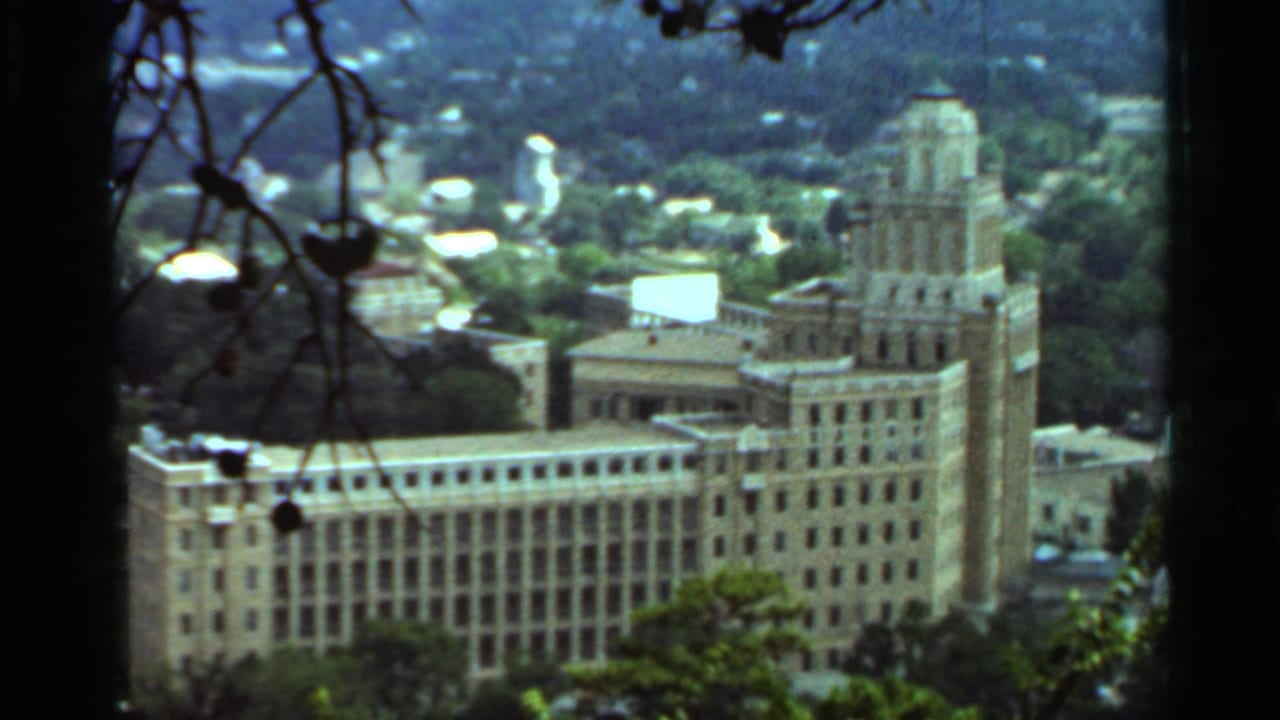 1965 Arkansas view of a large multi-story building with a prominent tower, seen from an elevated wooded vantage point.