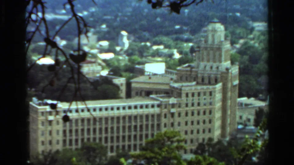 1965 Arkansas view of a large multi-story building with a prominent tower, seen from an elevated wooded vantage point.