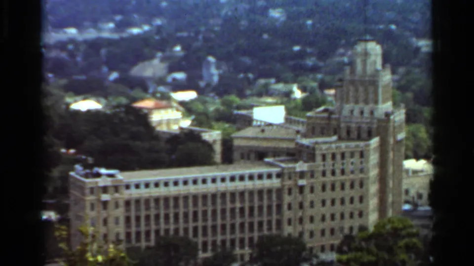 1965 Arkansas 8mm frame showing the large towered building from above, with trees, rooftops, and distant hills around it.