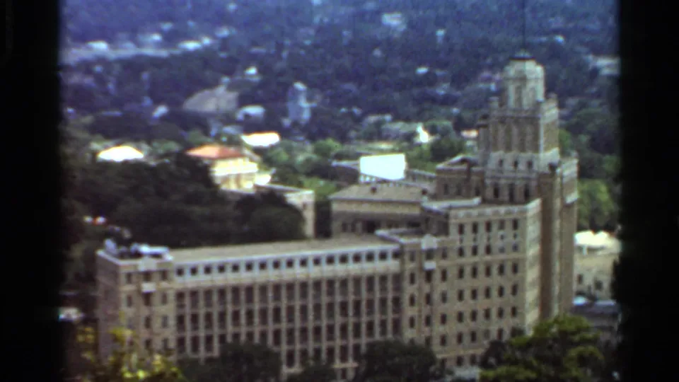 Final 1965 Arkansas frame of the towered building, with soft 8mm color, trees in front, and rooftops beyond.