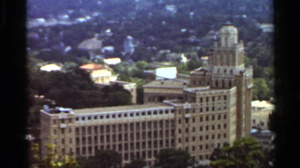 1965 Arkansas 8mm frame showing a large ornate building complex below a wooded overlook, with soft focus and saturated color.