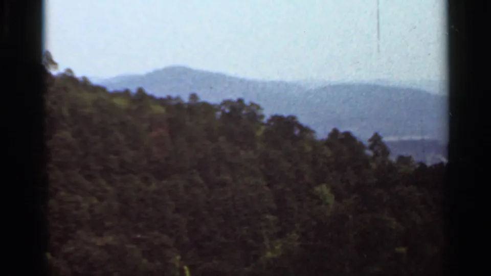 1965 Arkansas 8mm frame looking across forested hills toward hazy distant mountains beneath a bright sky.
