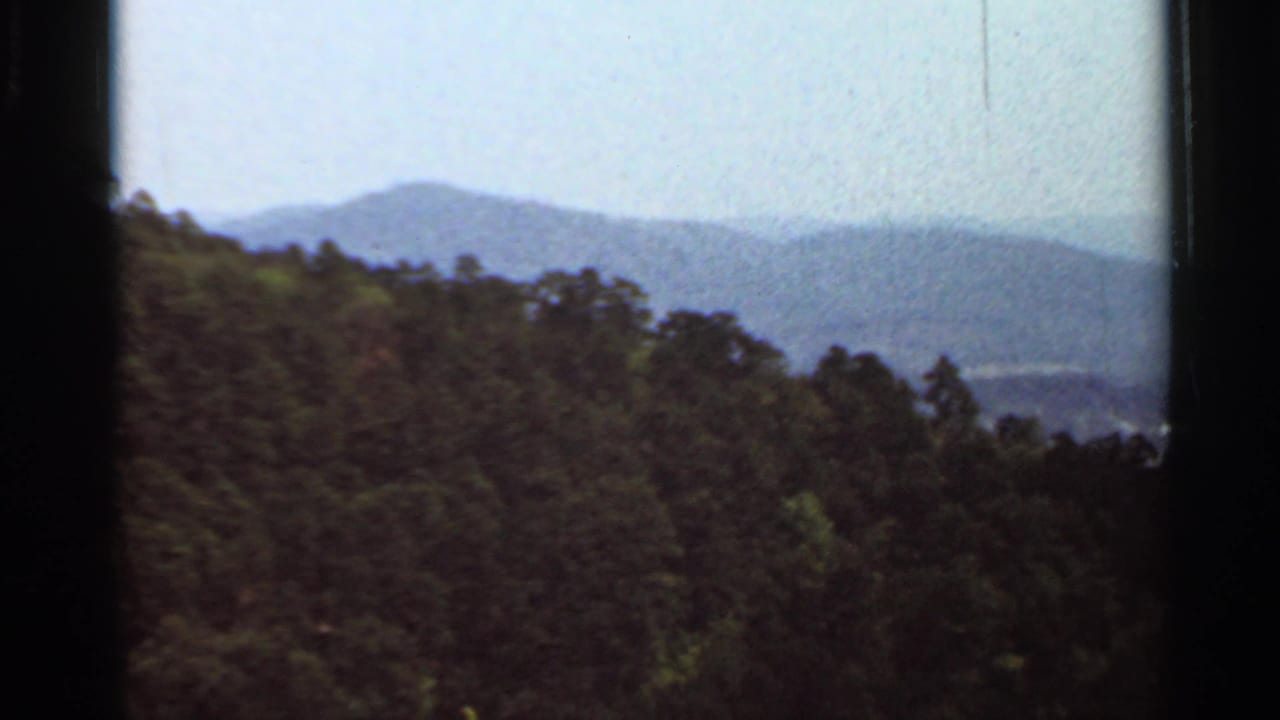 1965 Arkansas 8mm frame showing wooded hills, distant mountain ridges, and a pale hazy sky.