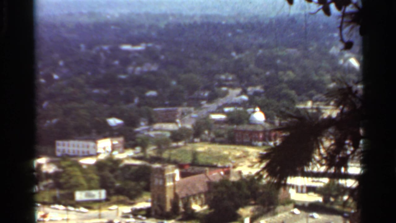 Aerial city view with church buildings, roads, trees, and commercial blocks.