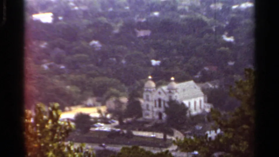 1965 Arkansas 8mm frame showing a white domed church, nearby road, and dense green trees from an elevated vantage point.