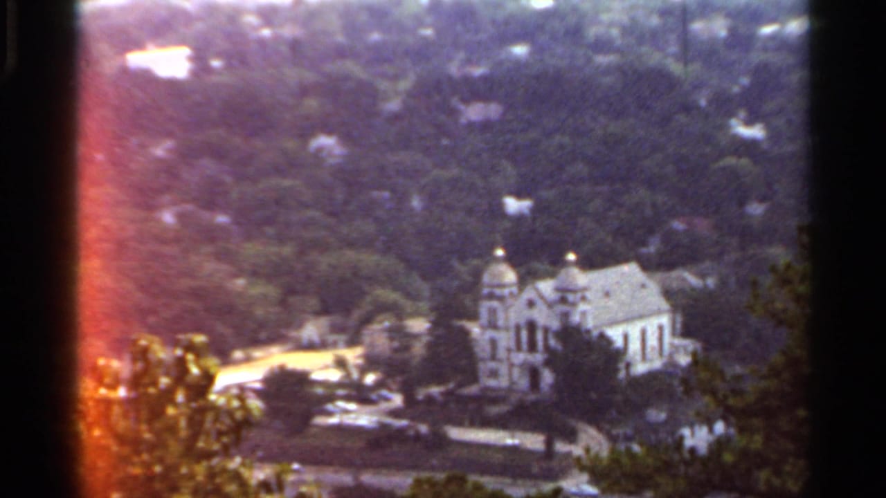 1965 Arkansas 8mm frame showing a white twin-domed building, likely a church or civic structure, viewed from above through trees.