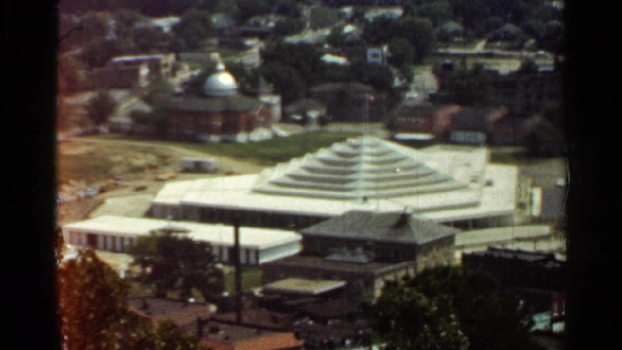 High-angle view of a modernist stepped-roof building among brick buildings and trees.