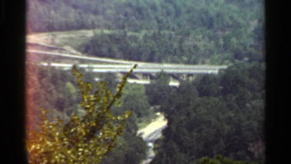 1965 Arkansas home-movie view of a highway overpass and forested valley, partly obscured by foreground foliage.