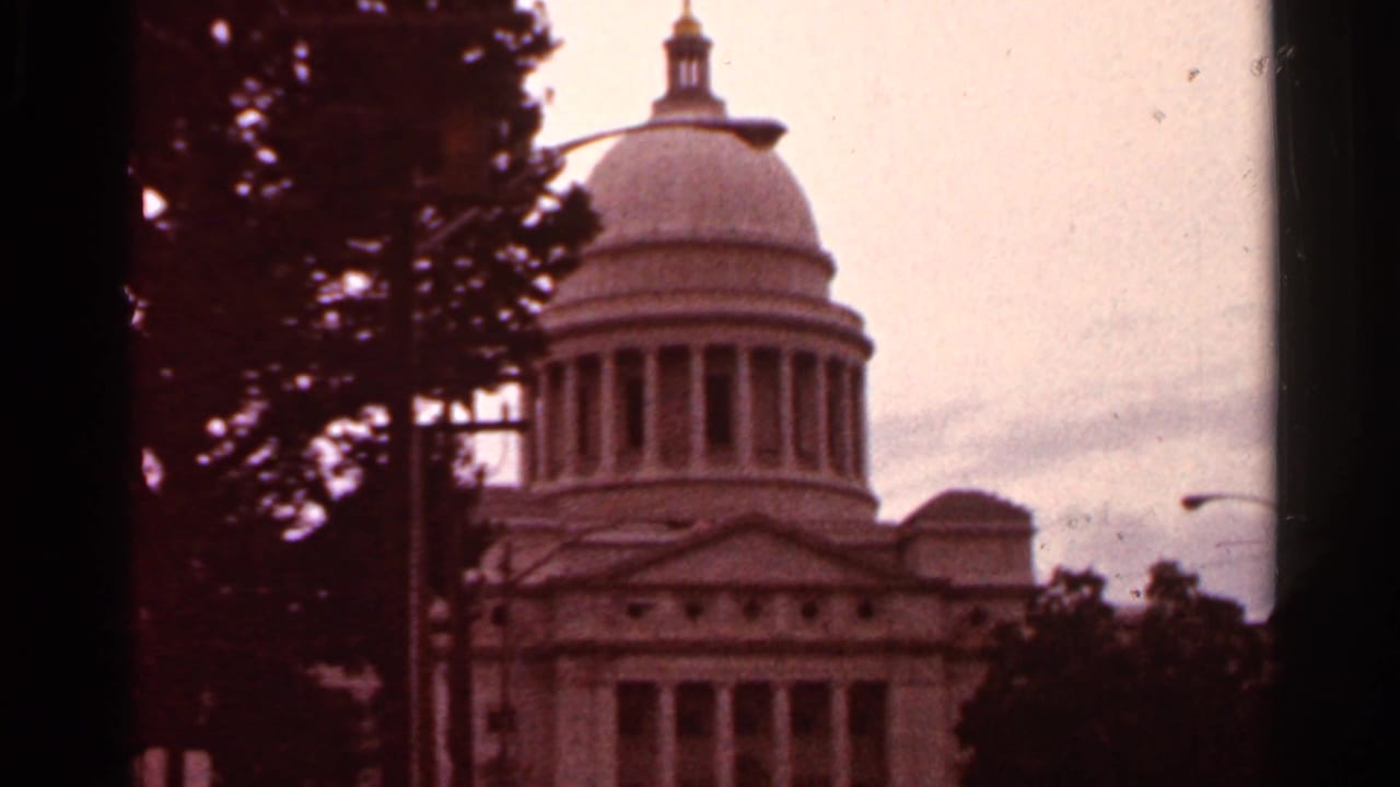 1965 8mm view in Arkansas of a domed capitol-style government building, seen through a dark window or gate edge.