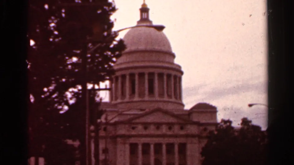 1965 8mm view in Arkansas of a domed capitol-style government building, seen through a dark window or gate edge.