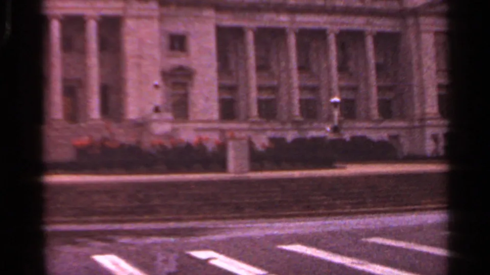 1965 Arkansas exterior of a columned civic building with landscaped grounds and street markings, filmed in soft 8mm color.