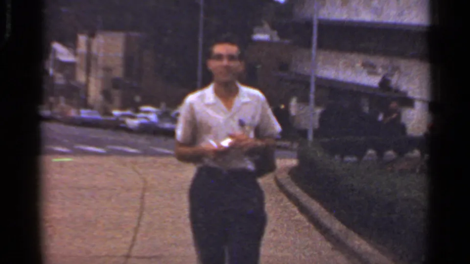 Adult man in a white short-sleeved shirt and dark trousers walks along a paved path in the Arkansas garden setting.